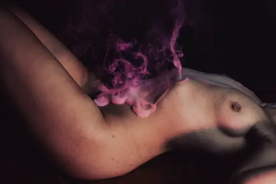 Nude torso and legs with pink smoke or vapor hovering over the abdomen, against a dark background.