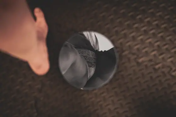 Foot near a small round mirror resting on a dark textured surface, reflecting a person wearing lace underwear.
