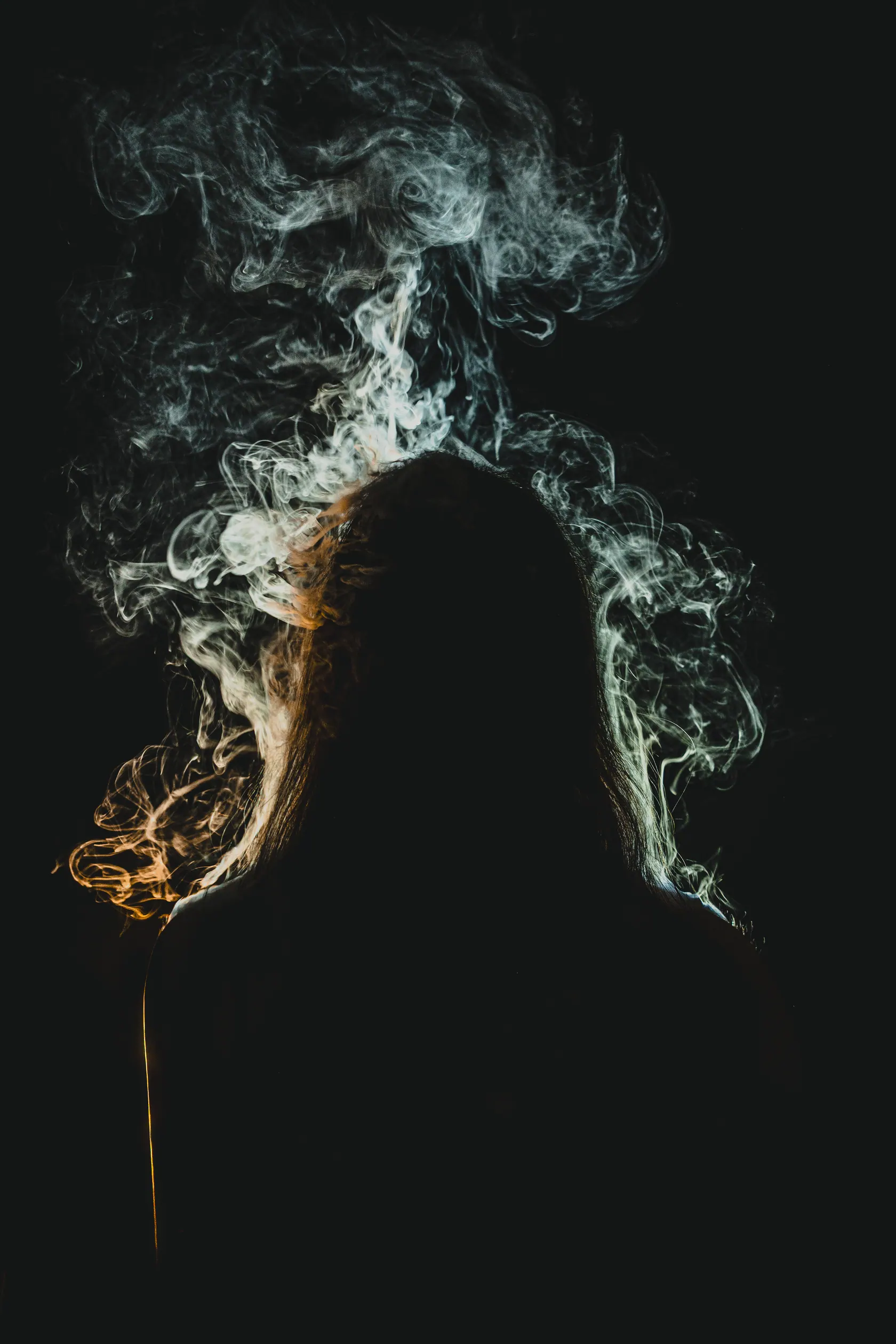 Silhouette of a person with long hair surrounded by swirling smoke against a dark background.